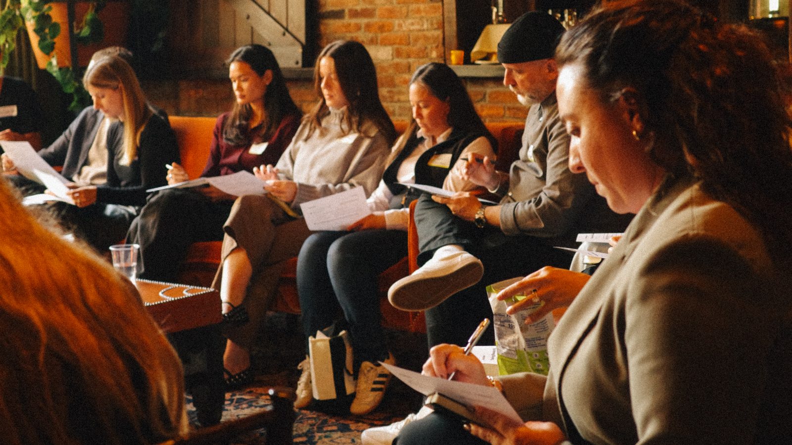Brand leaders seated along a brick wall at The Bowery Hotel, reading and writing on worksheets during the Customer Acquisition Playbook workshop