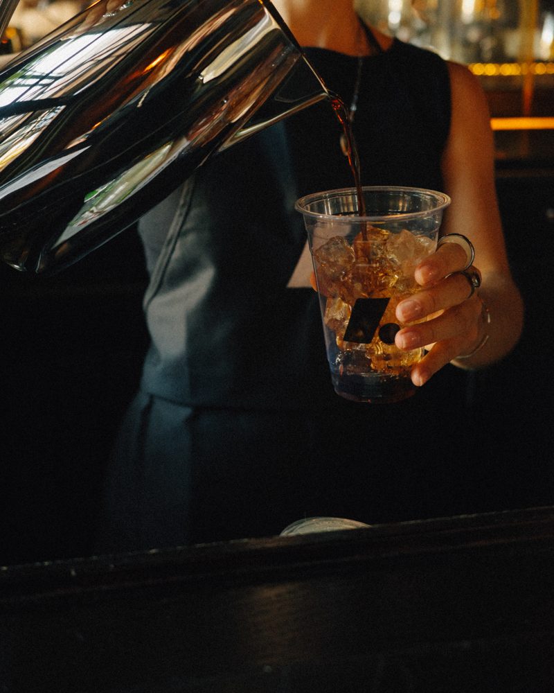 Iced coffee being poured into a cup printed with the Archive mark