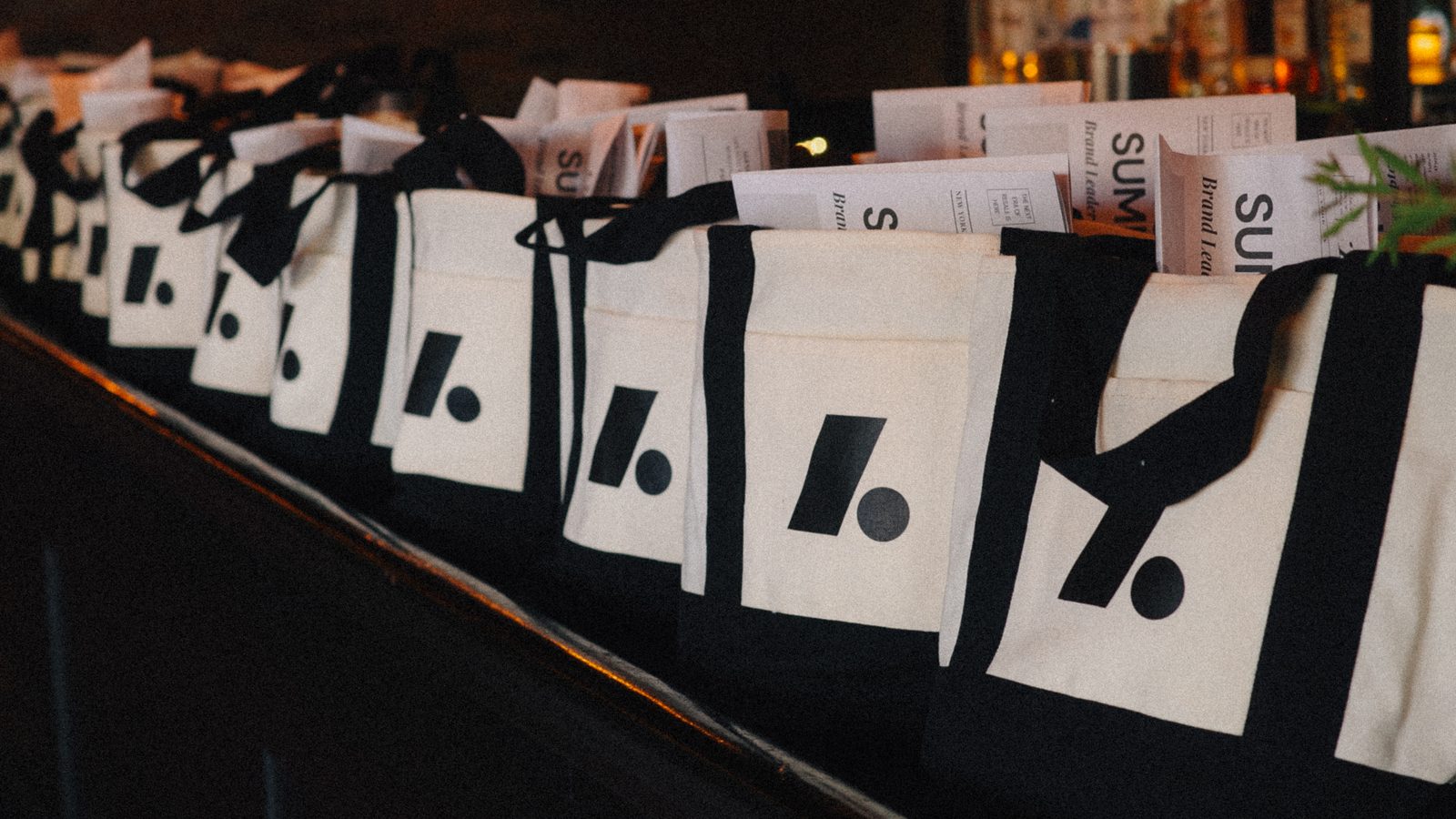 A row of Archive tote bags on the bar, each holding a printed copy of the summit agenda