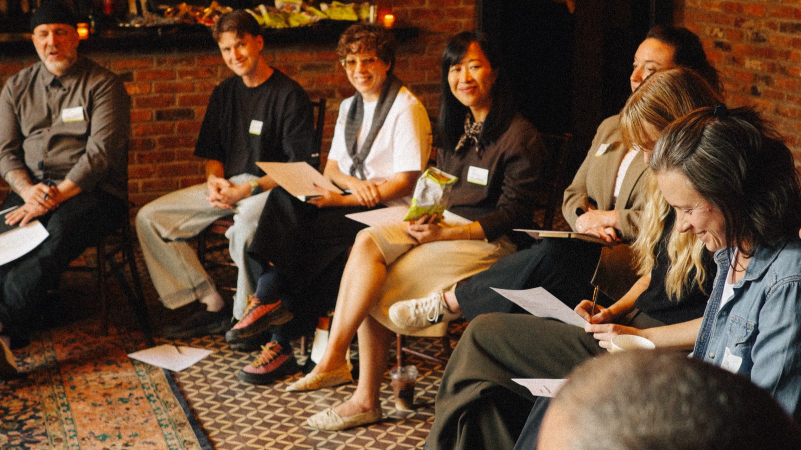 Attendees seated in a circle in a brick-walled room at The Bowery Hotel during the Taking Resale IRL workshop, smiling and taking notes