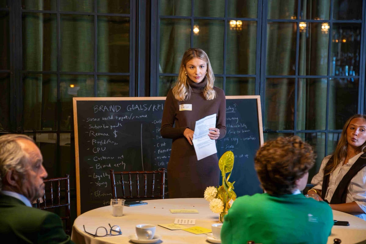 A speaker leading a roundtable discussion at a chalkboard